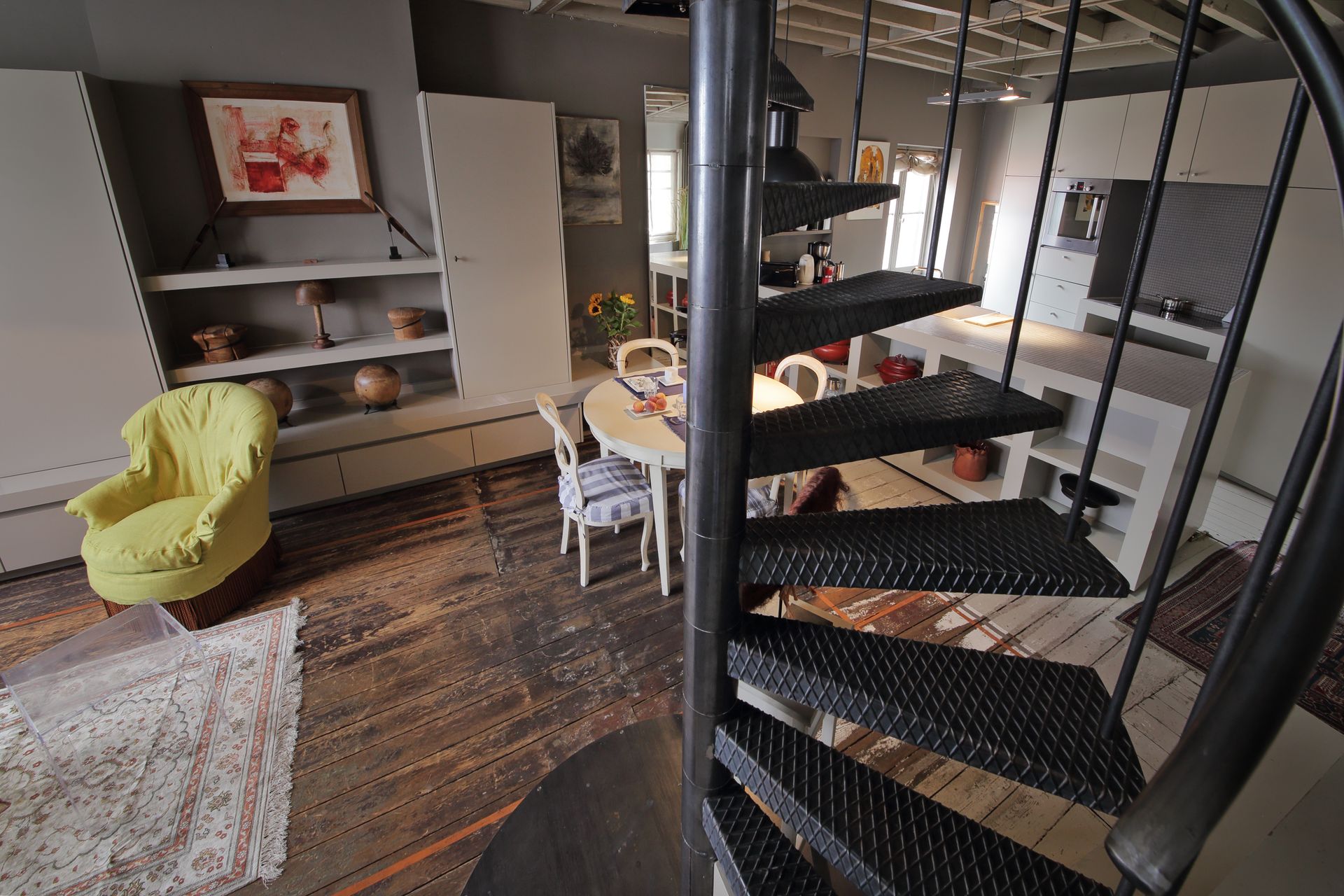 Salon loft moderne avec escalier en colimaçon noir, canapé gris, fauteuil jaune et grand tapis