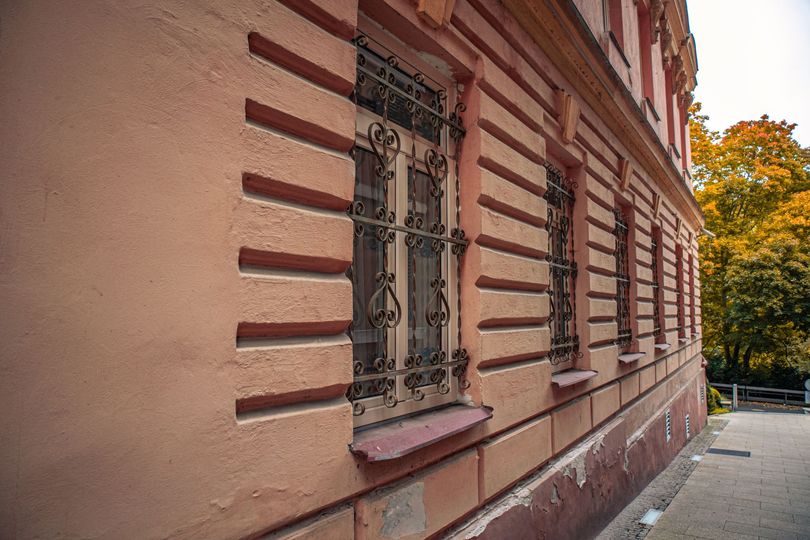 Façade rose d'un bâtiment historique avec des fenêtres à barreaux et des arbres d'automne le long d'une rue