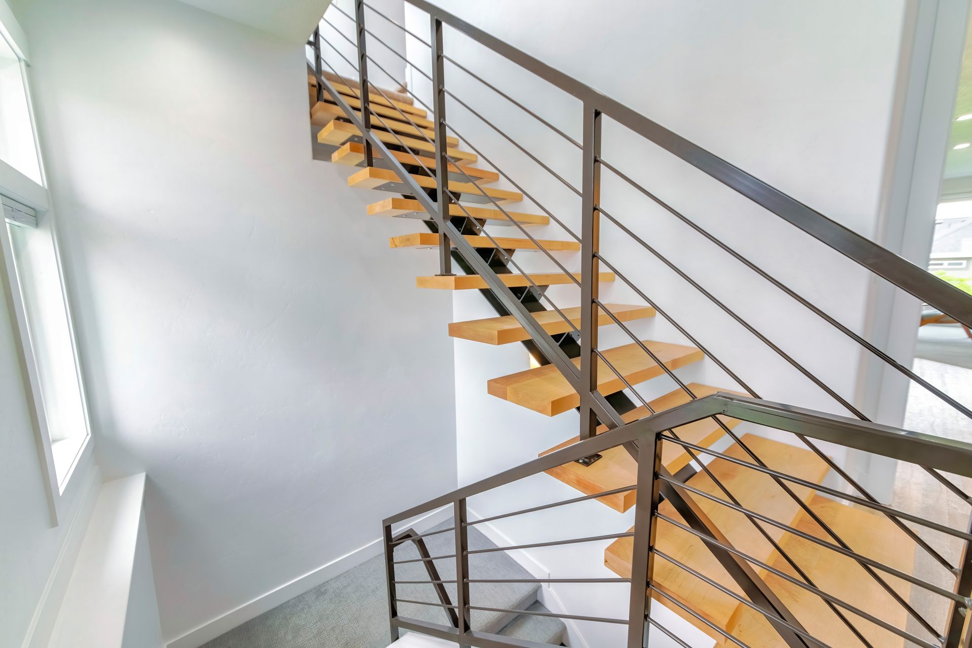Escalier intérieur moderne avec marches en bois, rampe en métal et grandes fenêtres laissant entrer la lumière.