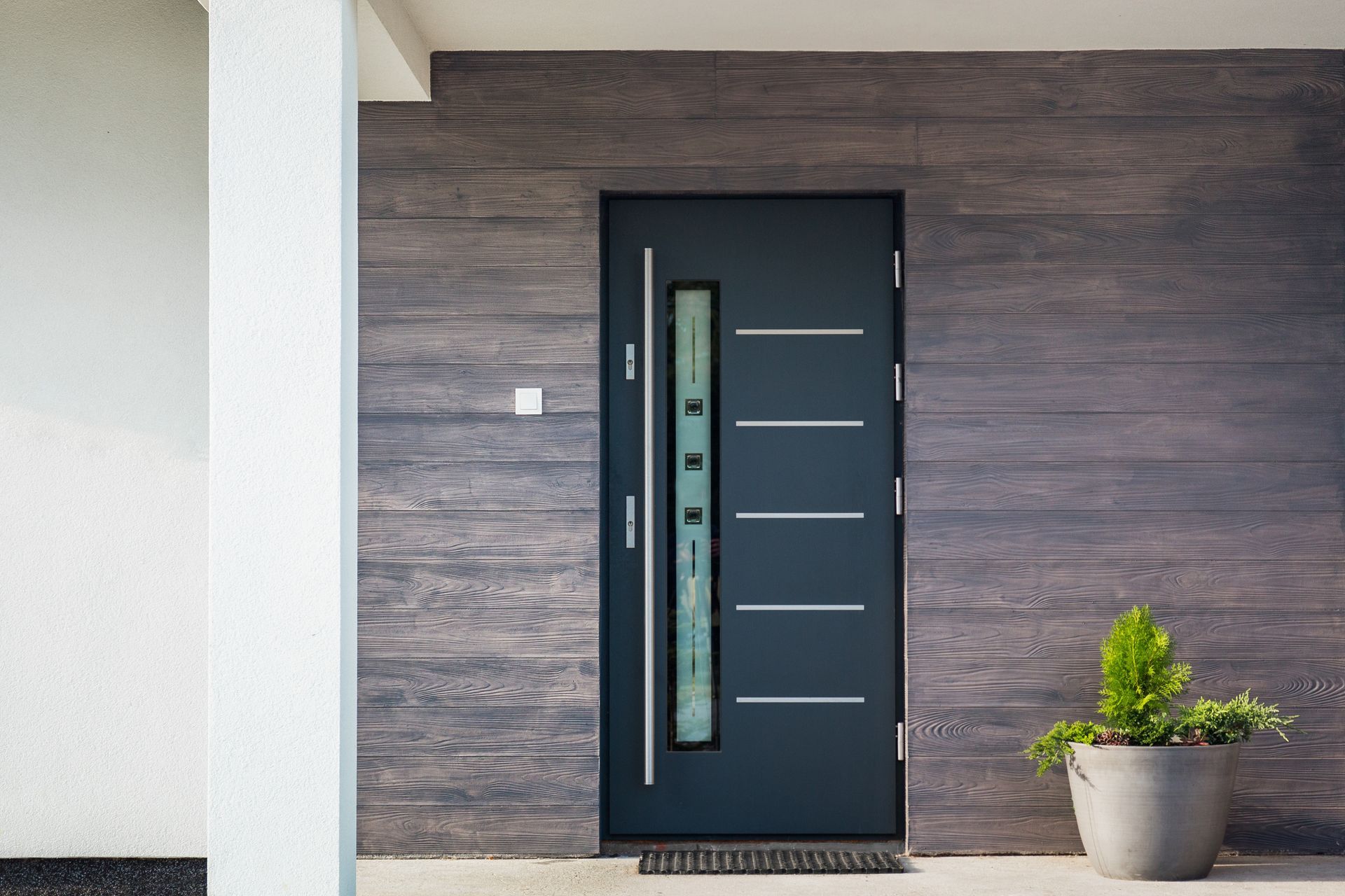 Porte d'entrée moderne avec insert en verre dépoli, encastrée dans un mur lambrissé à côté d'une plante en pot.