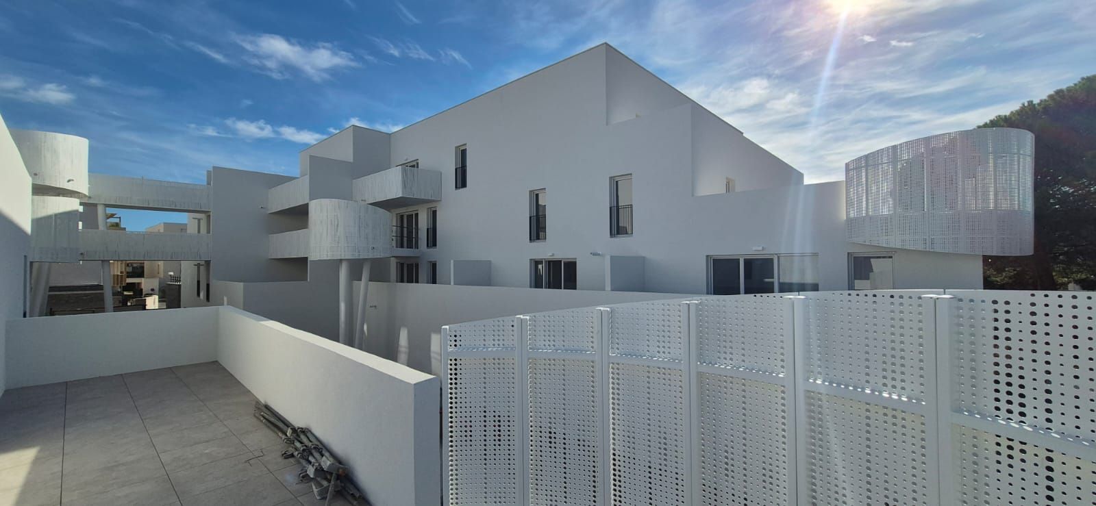 Des immeubles résidentiels blancs modernes derrière une clôture blanche sous un ciel radieux et ensoleillé