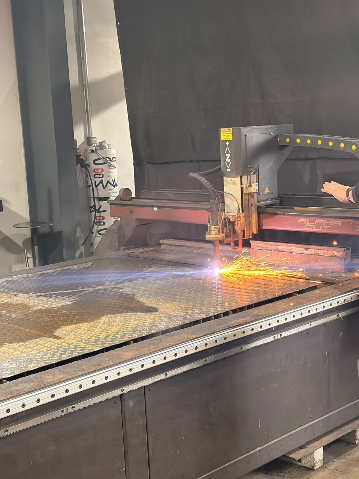 Machine de découpe industrielle tranchant du métal sur une table de travail, des étincelles jaillissent dans l'atelier.