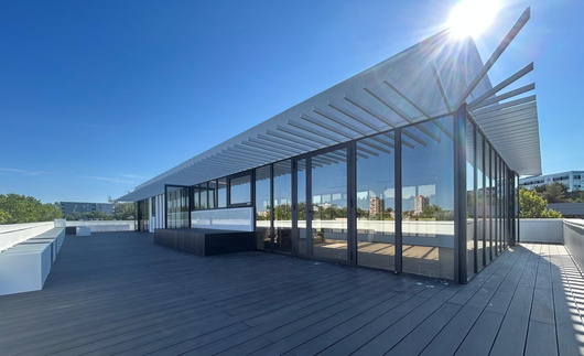 Terrasse moderne sur le toit avec parois vitrées, pergola à claire-voie et vue ensoleillée sur la ville