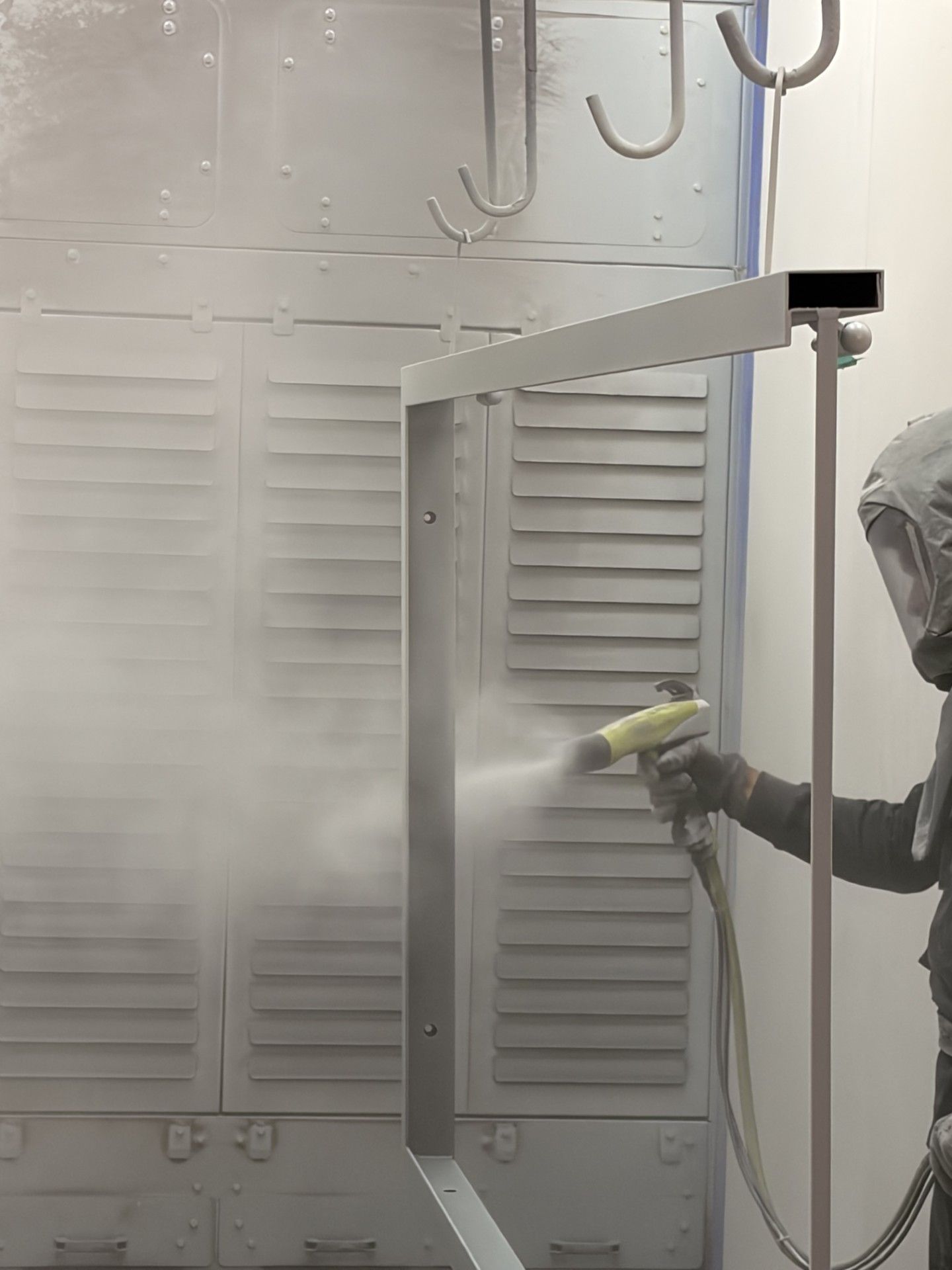 Une personne pulvérise de la peinture à l'intérieur d'une cabine à l'aide d'un pistolet à peinture, créant un nuage de brouillard.