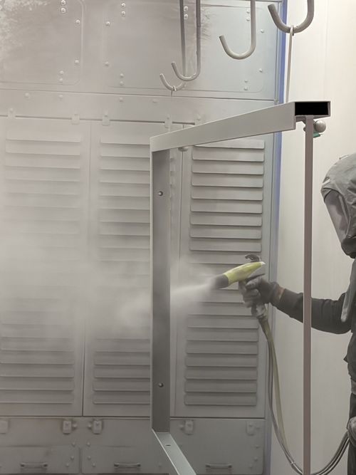 Une personne pulvérise de la peinture à l'intérieur d'une cabine à l'aide d'un pistolet à peinture, créant un nuage de brouillard.