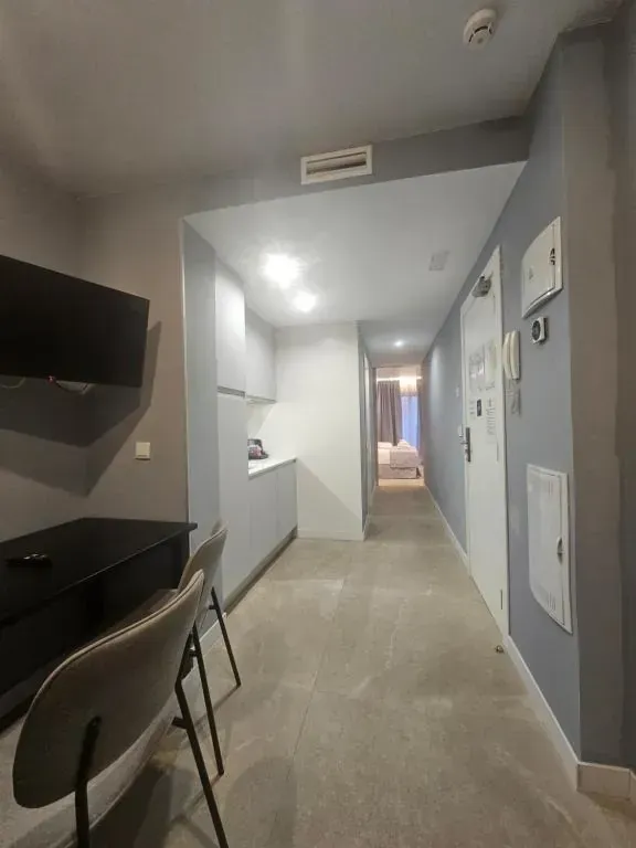 Pasillo estrecho del apartamento con cocina americana, escritorio y un dormitorio visible al fondo. 
