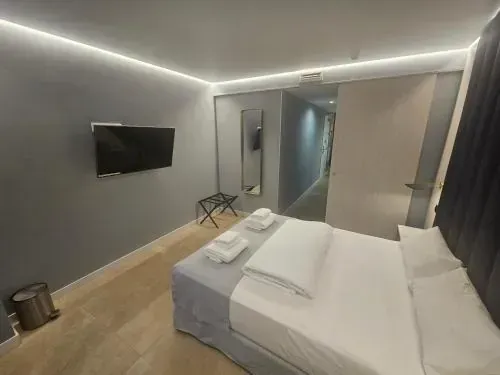Dormitorio con cama, televisor y puerta que da al pasillo. Paredes e iluminación grises.