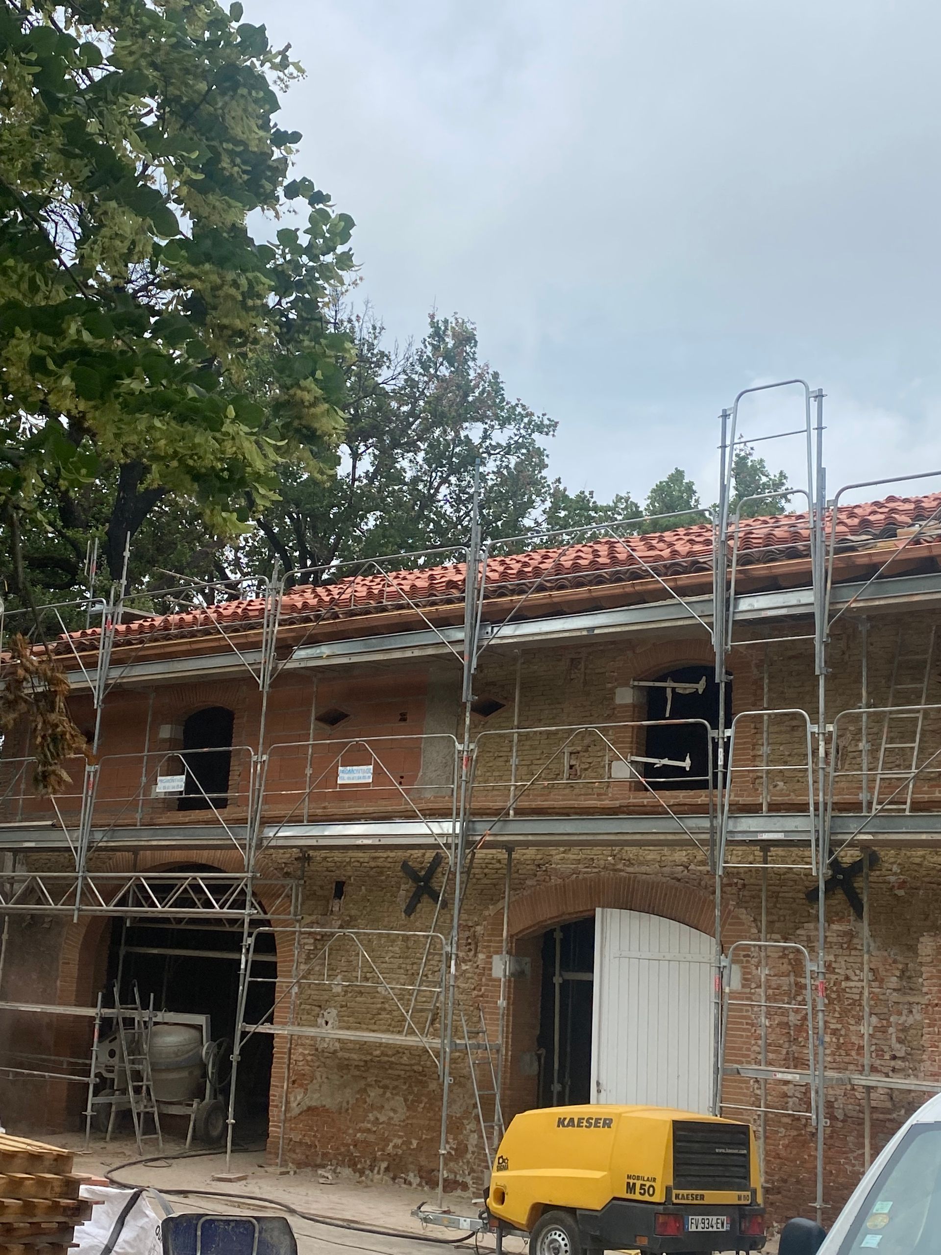 Bâtiment en rénovation avec échafaudages ; toit de tuiles rouges, murs en briques
