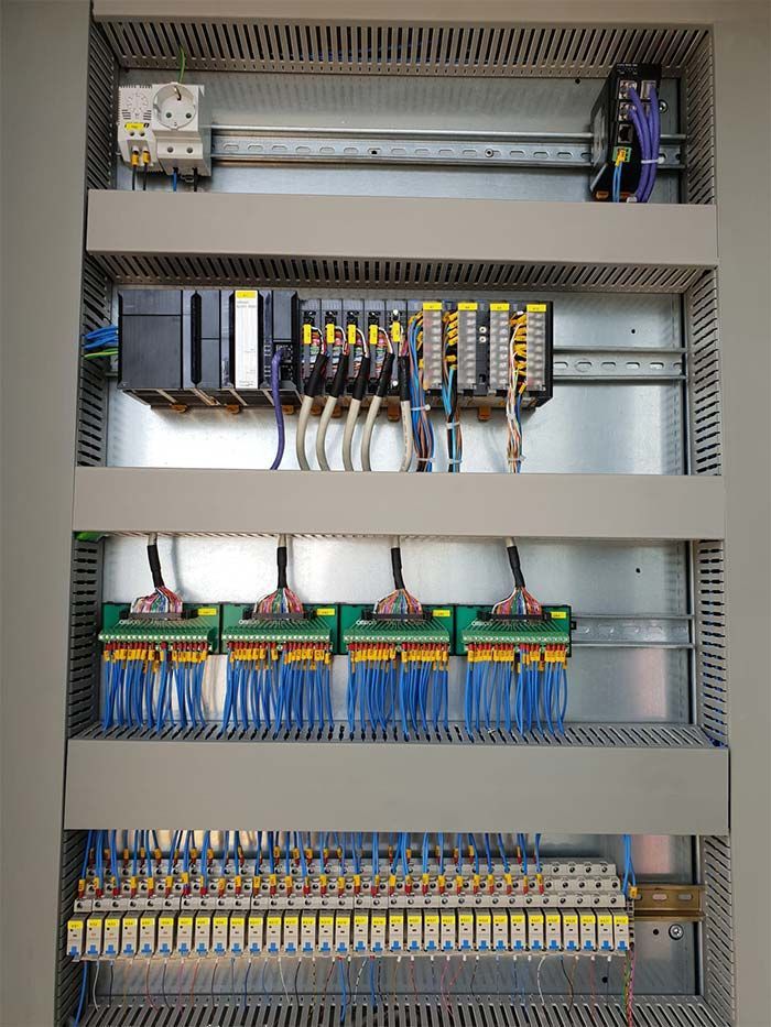 Panel de control eléctrico con filas de relés, cableado y bloques de terminales dentro de un gabinete metálico.