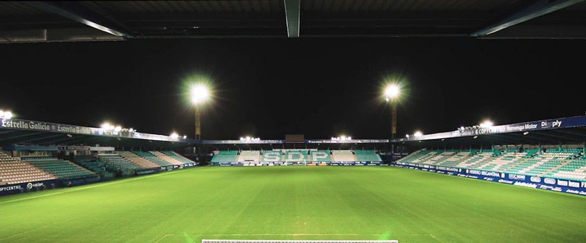 Vista panorámica de un estadio de fútbol vacío e iluminado por la noche, con un campo verde y gradas.