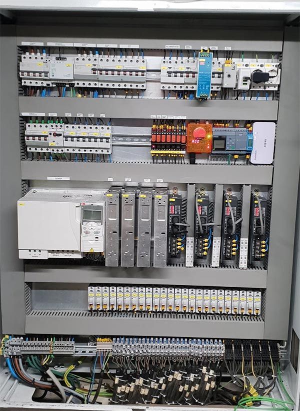 Panel de control eléctrico abierto con disyuntores, relés y cableado dentro de un gabinete metálico.