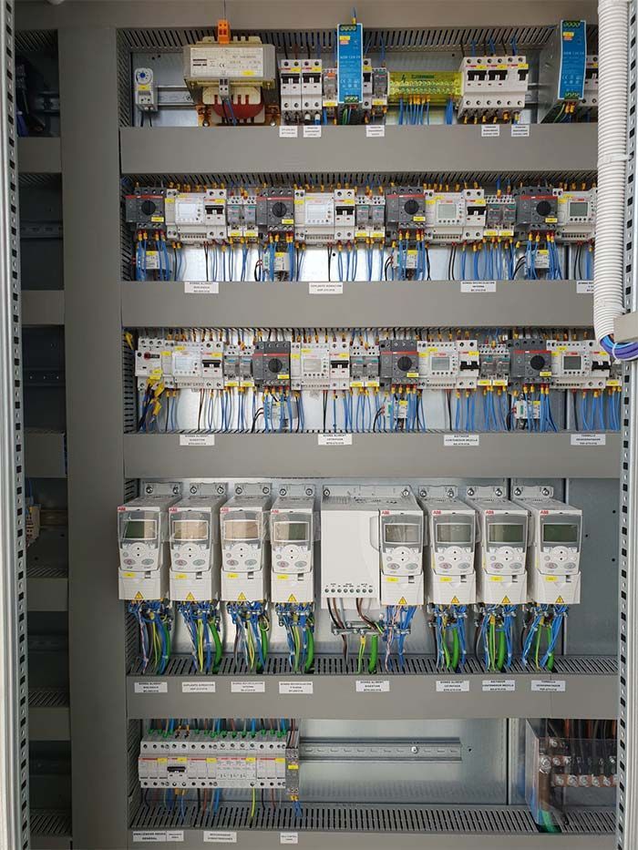 Panel de control eléctrico con filas de disyuntores, relés y cableado montados sobre rieles metálicos.