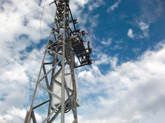 Trabajador de la torre sujeto con un arnés a una estructura metálica contra un cielo azul nublado.