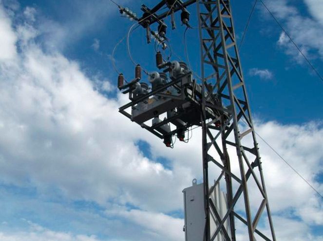 Trabajadores de servicios públicos en una plataforma de líneas eléctricas junto a una torre metálica contra un cielo azul