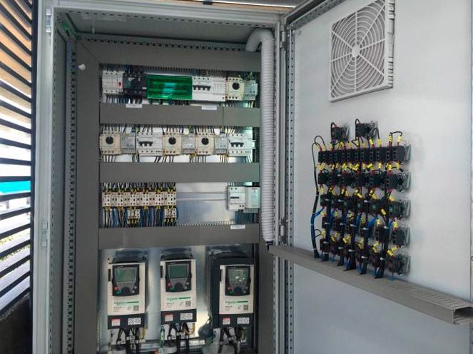 Armario de control eléctrico abierto con disyuntores, relés y cableado en su interior.