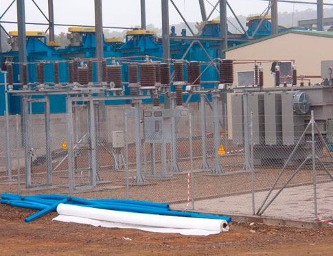 Patio industrial cercado con equipos azules, tanques de metal y tuberías blancas enrolladas en el suelo.