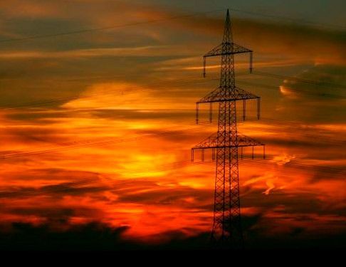 Silueta de una torre de transmisión eléctrica contra un espectacular cielo de atardecer naranja rojizo.