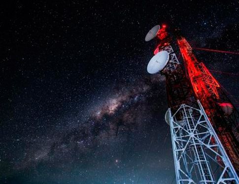 Torre de comunicaciones iluminada en rojo bajo un cielo nocturno estrellado con la Vía Láctea visible.