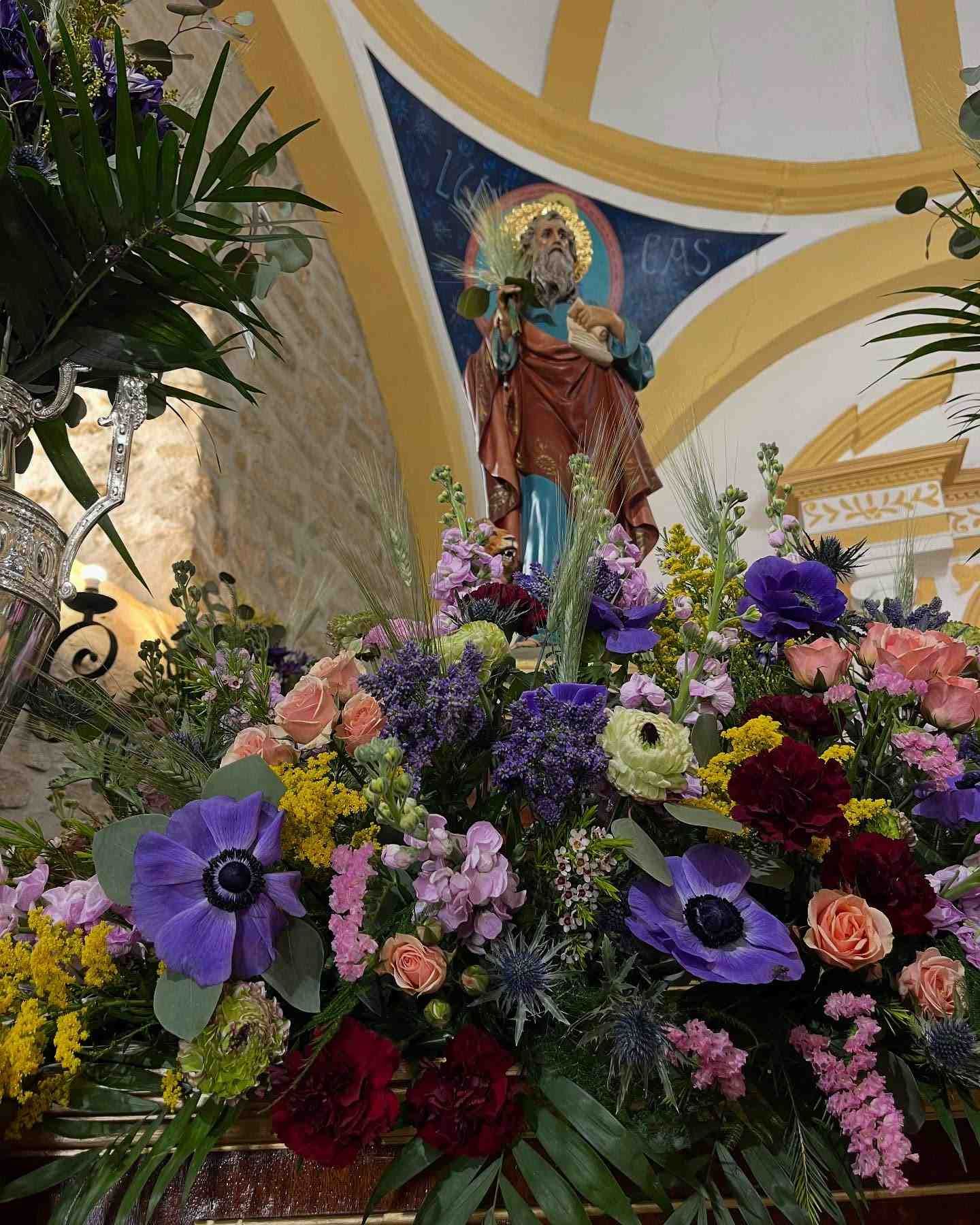 Estatua de un santo rodeada de flores de colores, dentro de una iglesia.