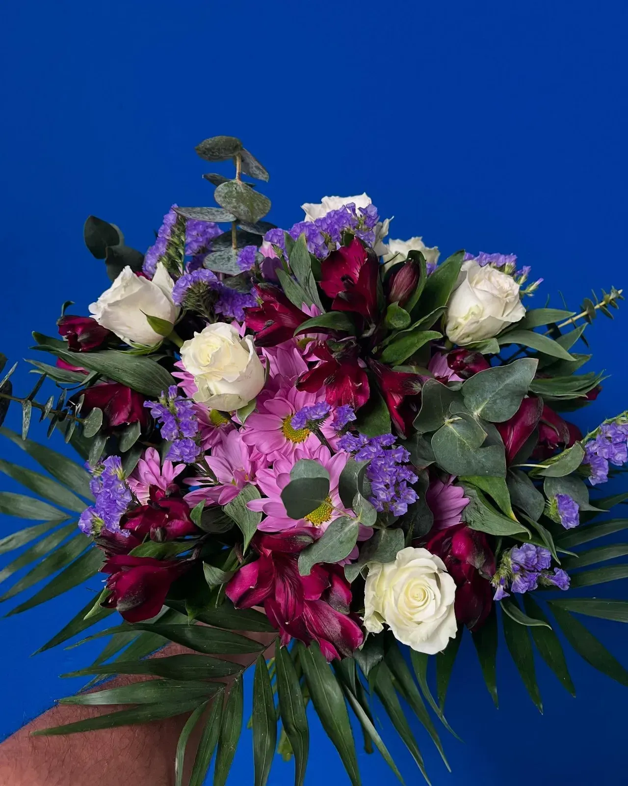 Ramo de rosas blancas, flores de color rojo intenso, flores de color púrpura y follaje verde sobre un fondo azul.