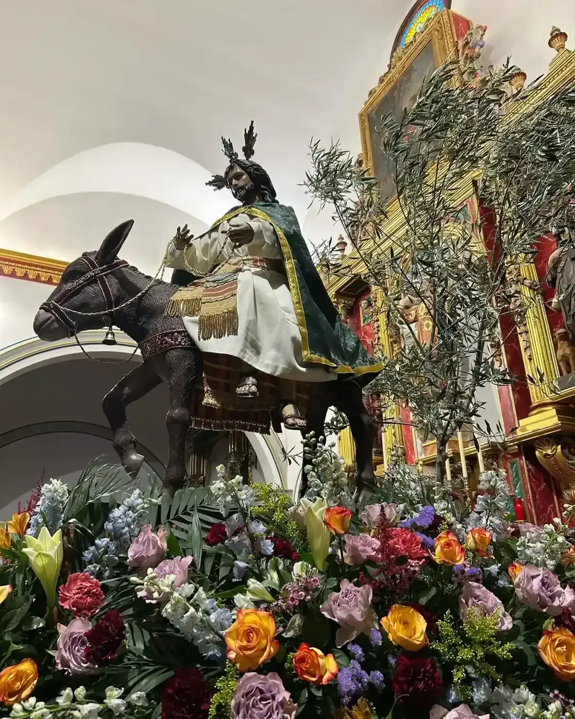 Estatua de Jesús sobre un burro, rodeado de flores, en una iglesia.