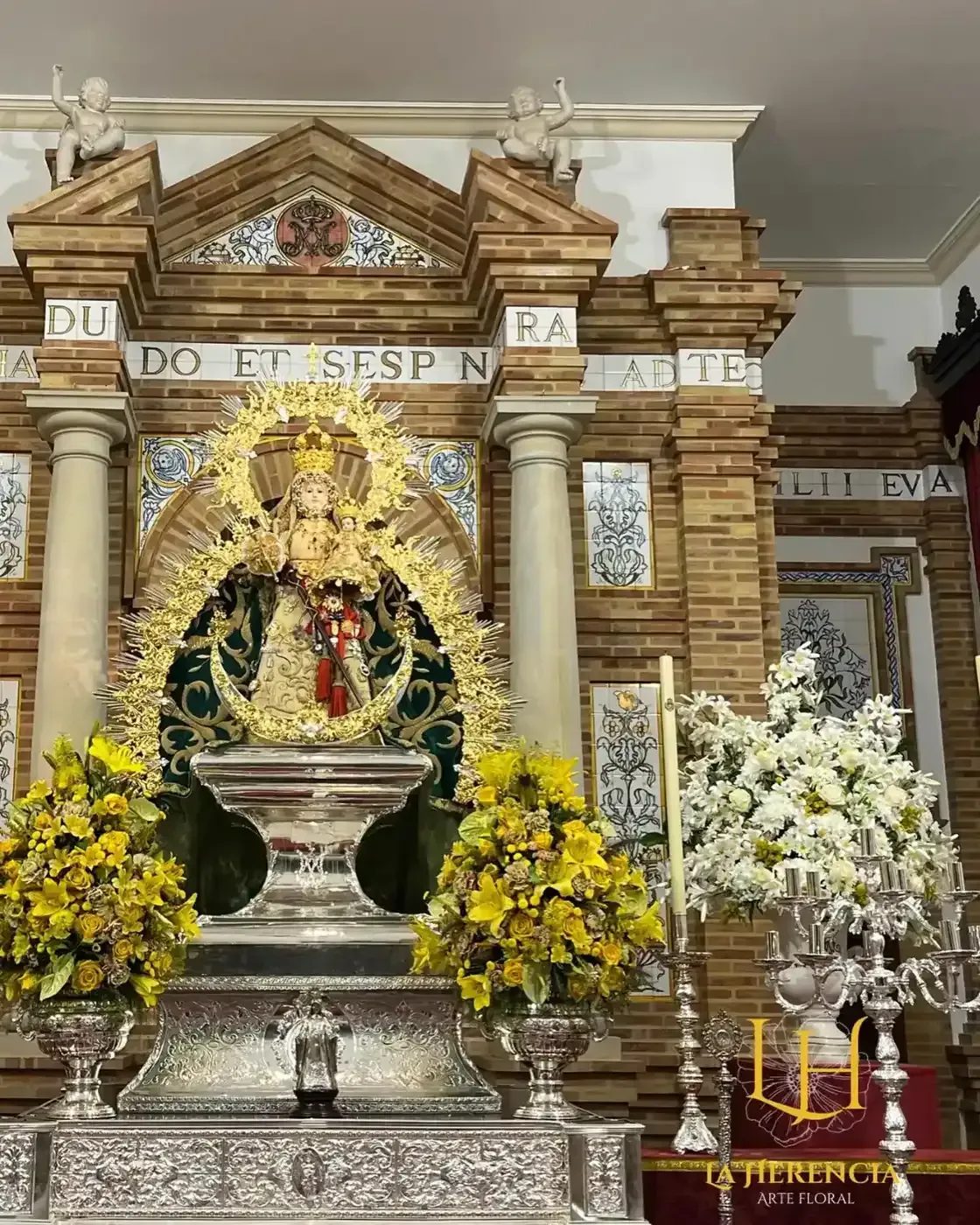 Altar con una estatua de la Virgen María con el Niño Jesús, adornada con oro y rodeada de flores.