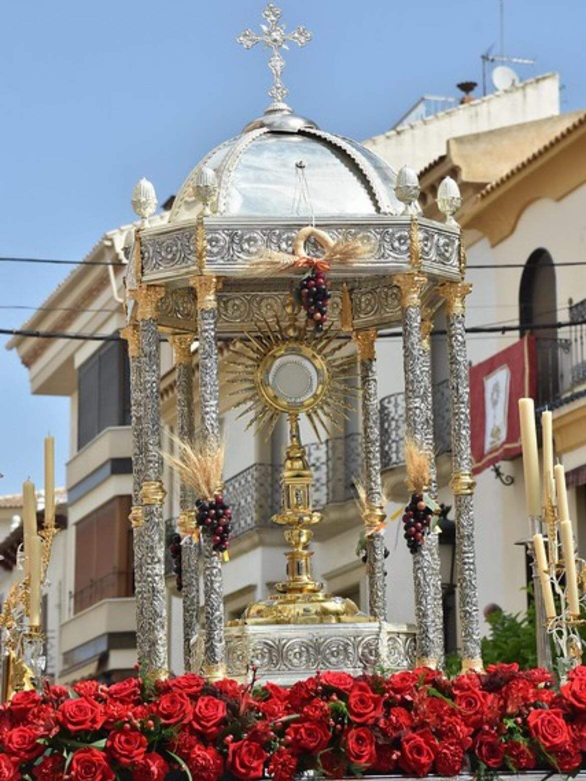 Custodia ornamentada que contiene la Eucaristía en procesión, decorada con rosas rojas y columnas.