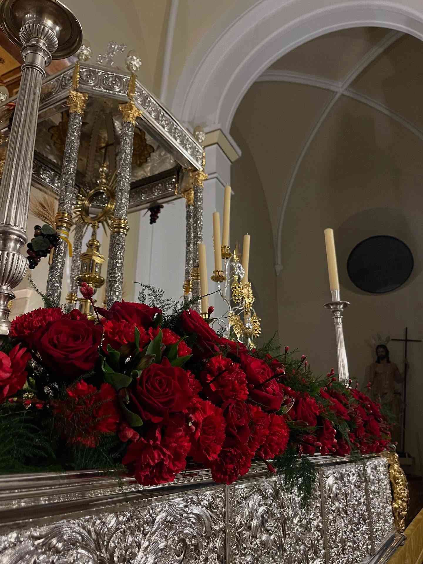 Estructura ornamentada de plata adornada con flores rojas y velas en una iglesia.