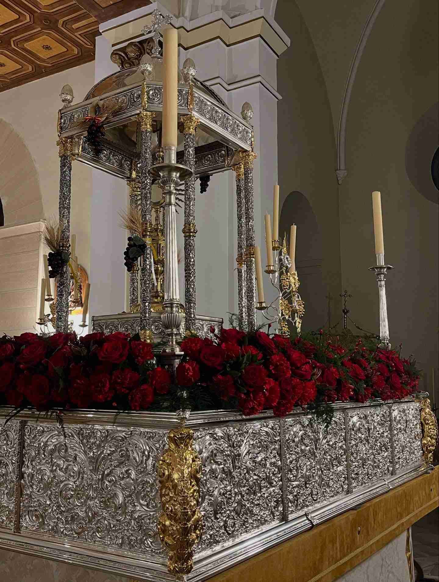Exhibición religiosa de plata con rosas rojas y velas dentro de una iglesia.