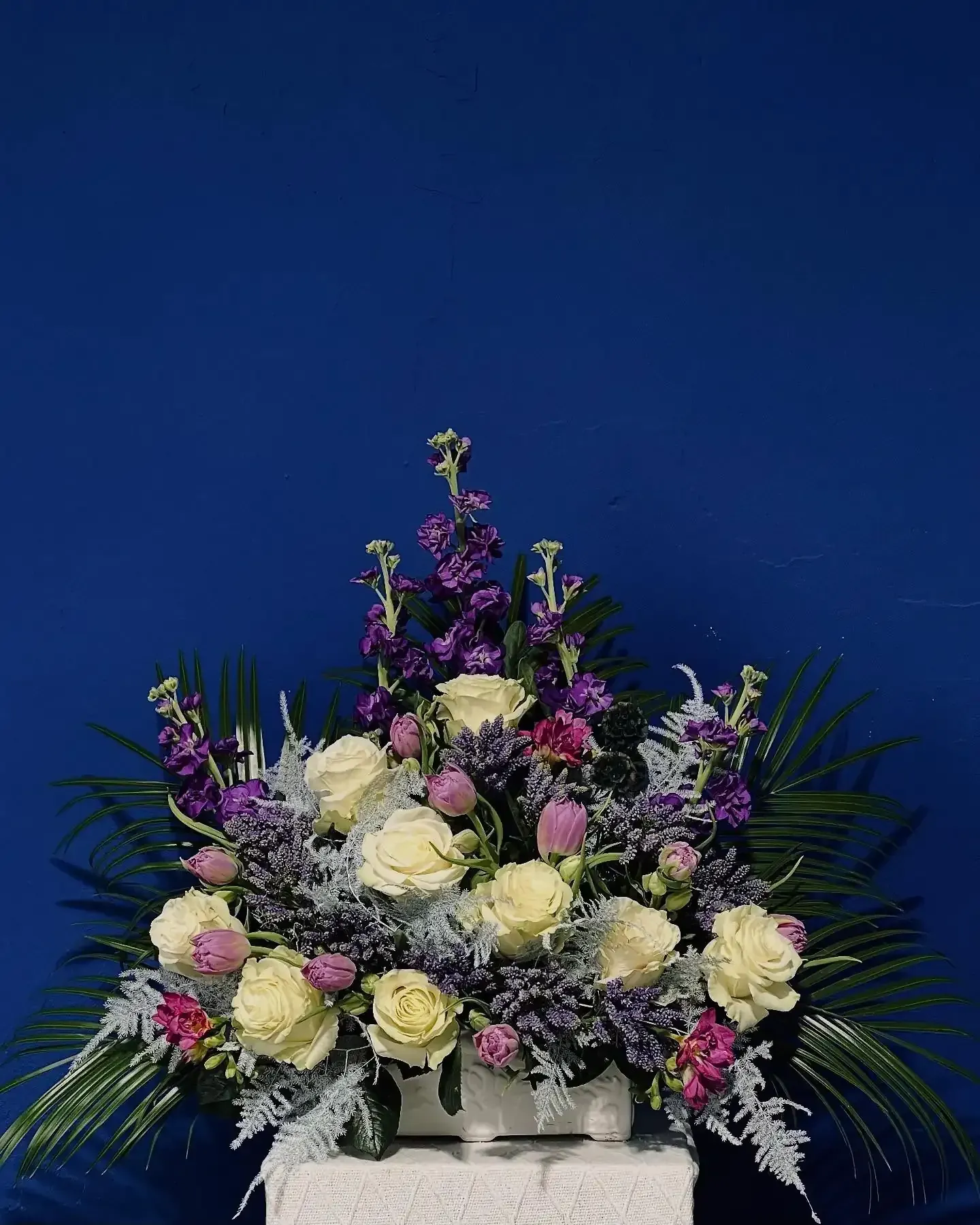 Arreglo floral de rosas blancas y alhelíes morados sobre fondo azul.