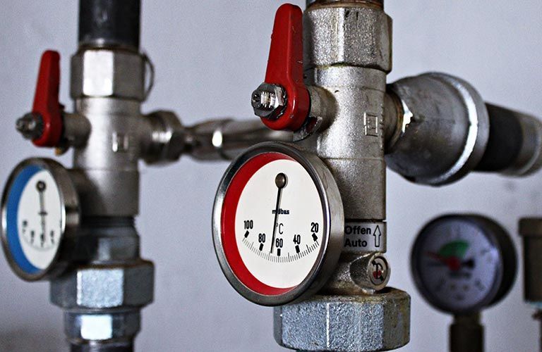 Tuyaux équipés de manomètres et de vannes à poignée rouge, affichant les relevés de température et autres paramètres.