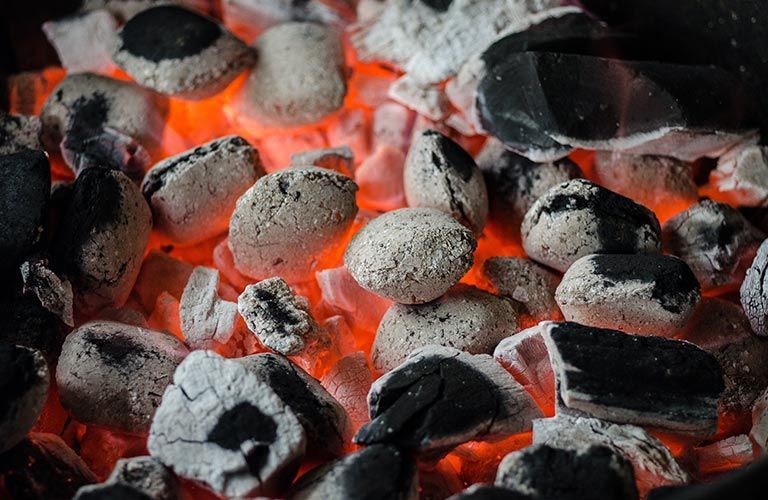 Briquettes de charbon incandescentes, braises rouge-orangé en dessous.