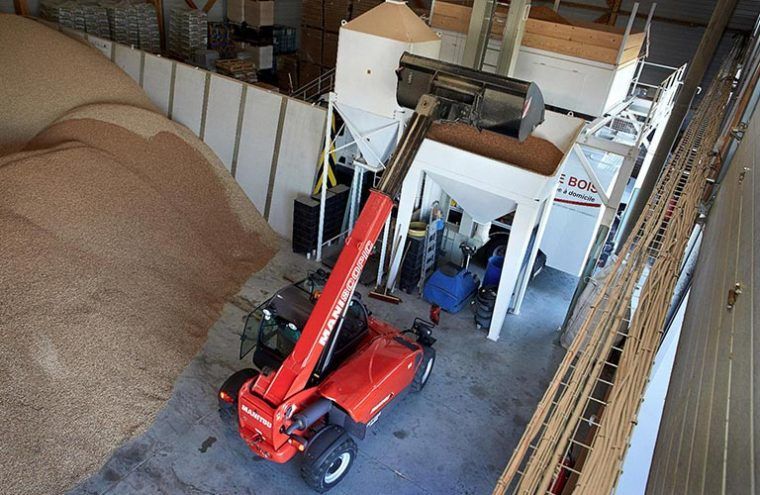 Un chariot élévateur rouge charge des céréales dans des machines d'un entrepôt.