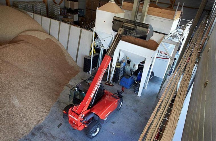 Un chariot élévateur rouge charge des céréales dans des machines d'un entrepôt.