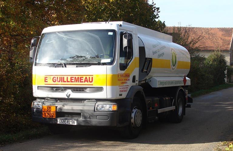 Camion-citerne blanc, immatriculé « E. Guillemeau », sur une route, avec des touches de jaune. Paysage rural.