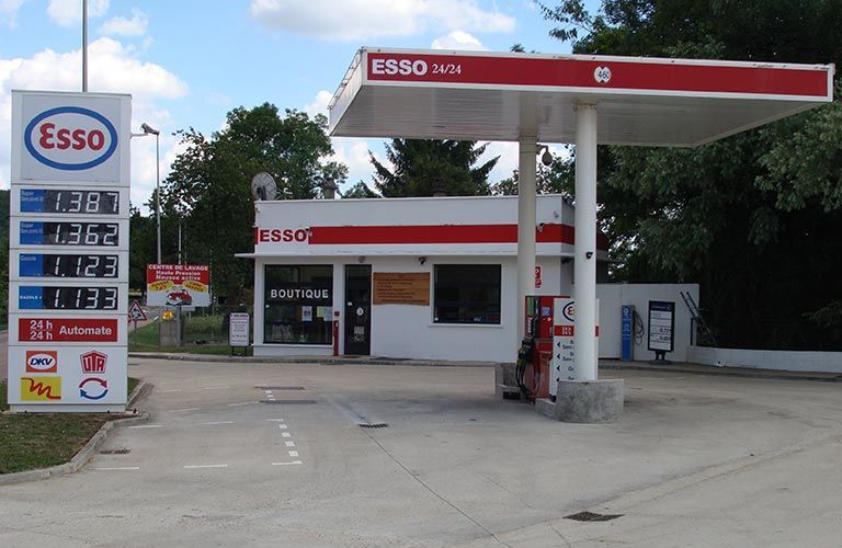 Une station-service Esso avec affichage des prix, dotée d'un auvent rouge et blanc et d'une petite boutique.