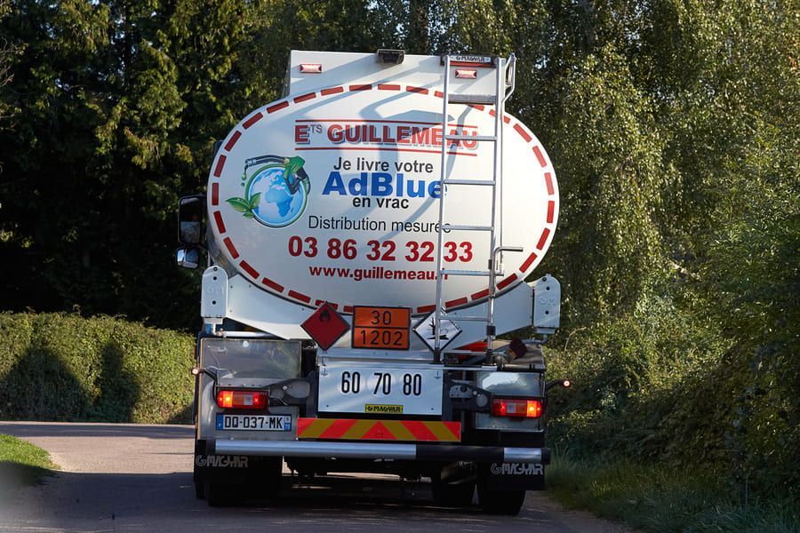 Camion-citerne à carburant AdBlue publicitaire circulant sur une route.