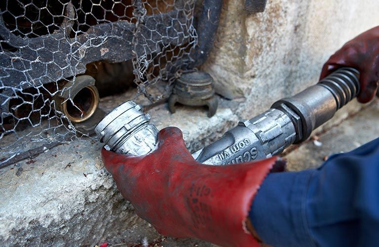 La personne portant un gant rouge raccorde un embout de carburant argenté à un raccord en laiton.