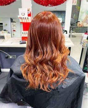 Una mujer con cabello largo y rojo está sentada en una silla en un salón.