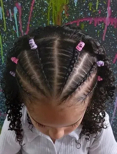 Una niña con cabello rizado y trenzas lleva una camisa blanca.