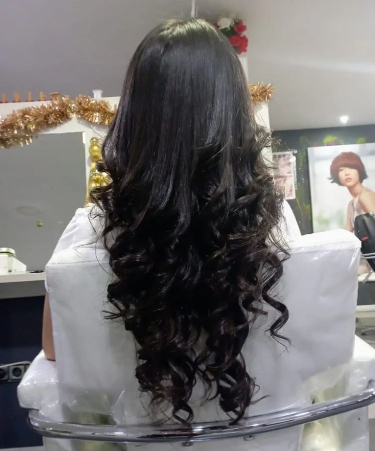 Una mujer con cabello largo y rizado está sentada en una silla en un salón.