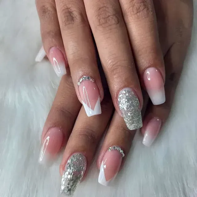 Un primer plano de las uñas de una mujer con manicura francesa y pedrería.