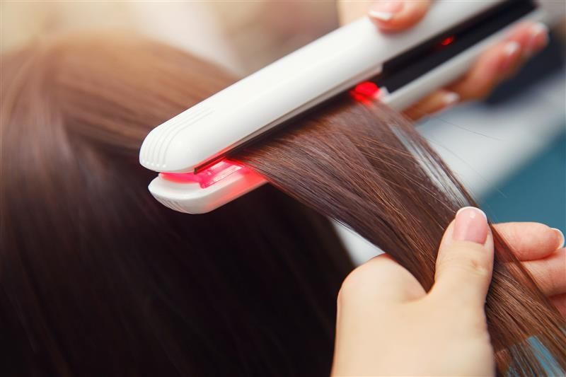 Una mujer se está alisando el cabello con una plancha.