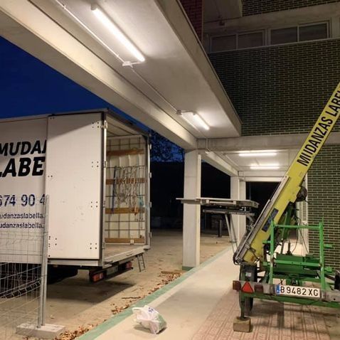 Camión de mudanzas con las puertas abiertas junto a un edificio; grúa extendida. Etiqueta 