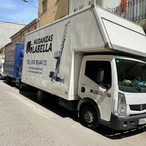 Dos camiones de mudanzas estacionados en una calle; un camión blanco tiene el logo de 