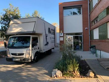 Camión de mudanzas blanco estacionado frente a la entrada de un edificio de ladrillo.