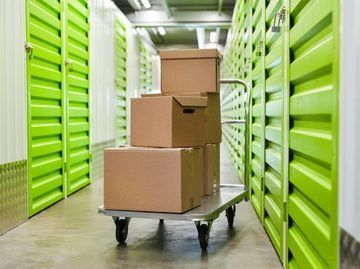 Cajas apiladas en un carrito en el pasillo de una unidad de almacenamiento con puertas verdes.