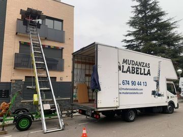Camión de mudanzas con elevador, cargando muebles en un edificio.