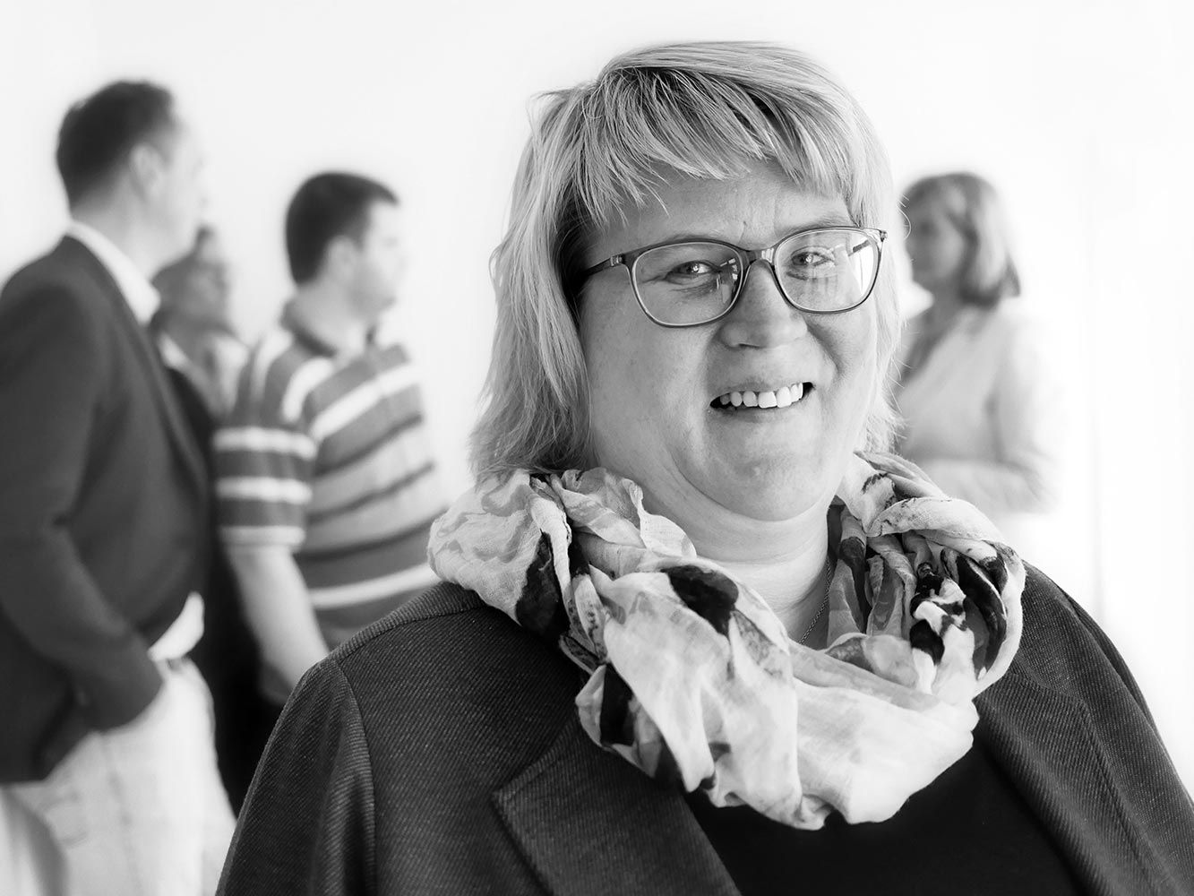 eine Frau mit Brille und Schal lächelt in einem Schwarz-Weiß-Foto .
