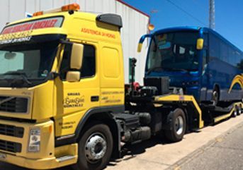 Un camión amarillo remolca un autobús azul en un remolque.